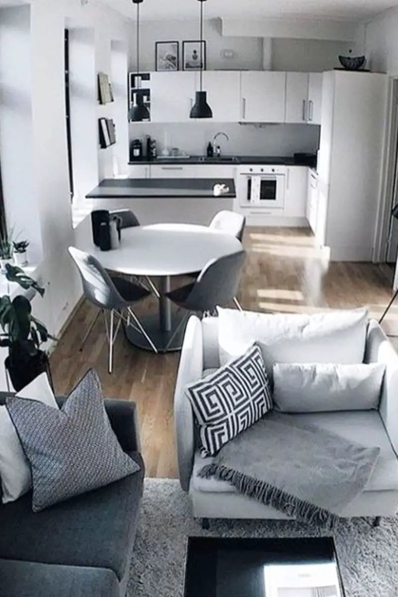 cosy grey living room inside a tiny house with open floor plan showing modern white kitchen and eating area with neutral wood floors throughout