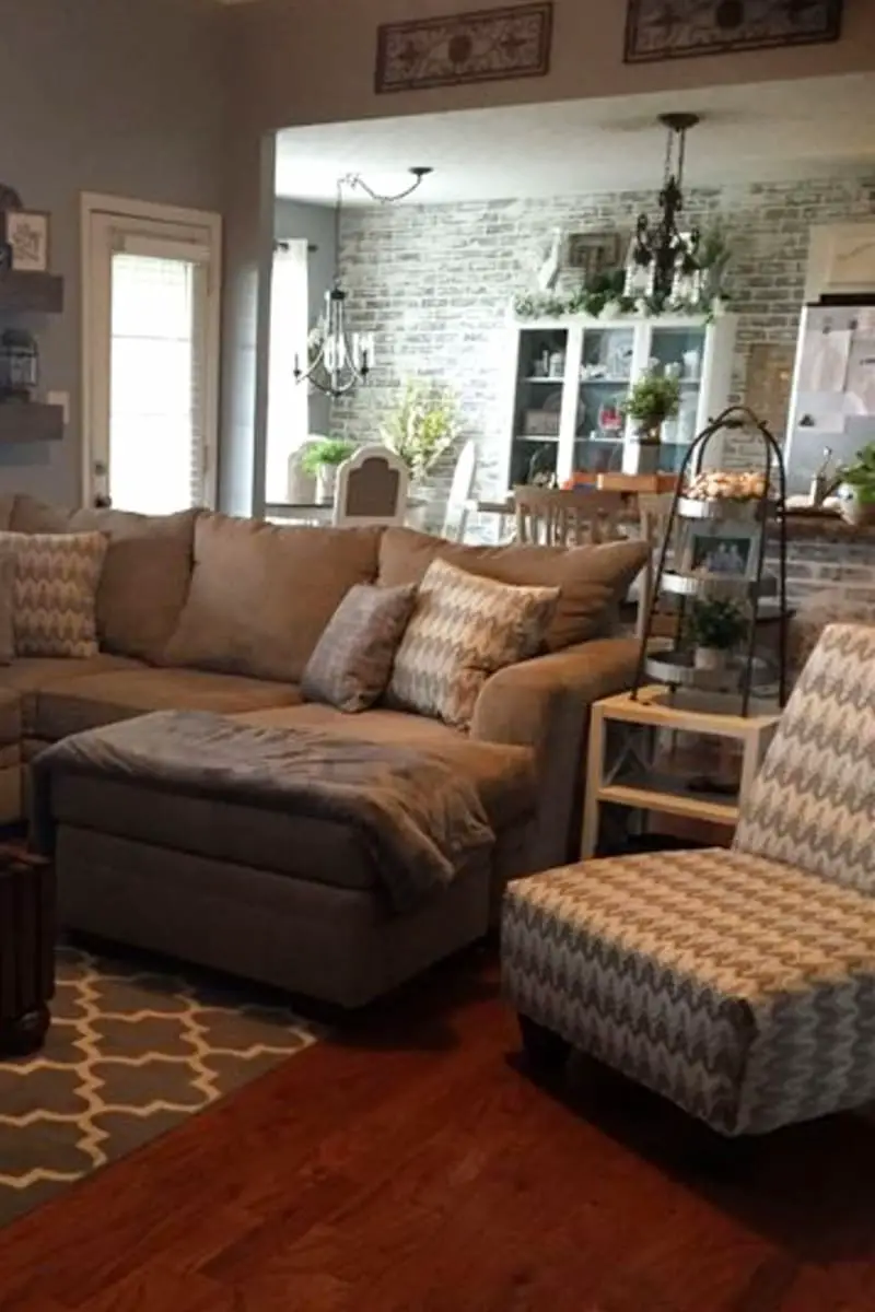 Neutral cozy grey living room with patterned accent chair and throw pillows, grey and white area rug and brick accent wall